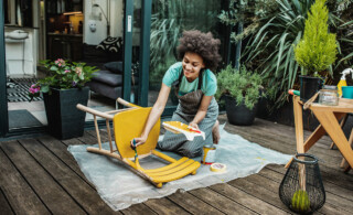 Young woman repainting wooden chair on patio