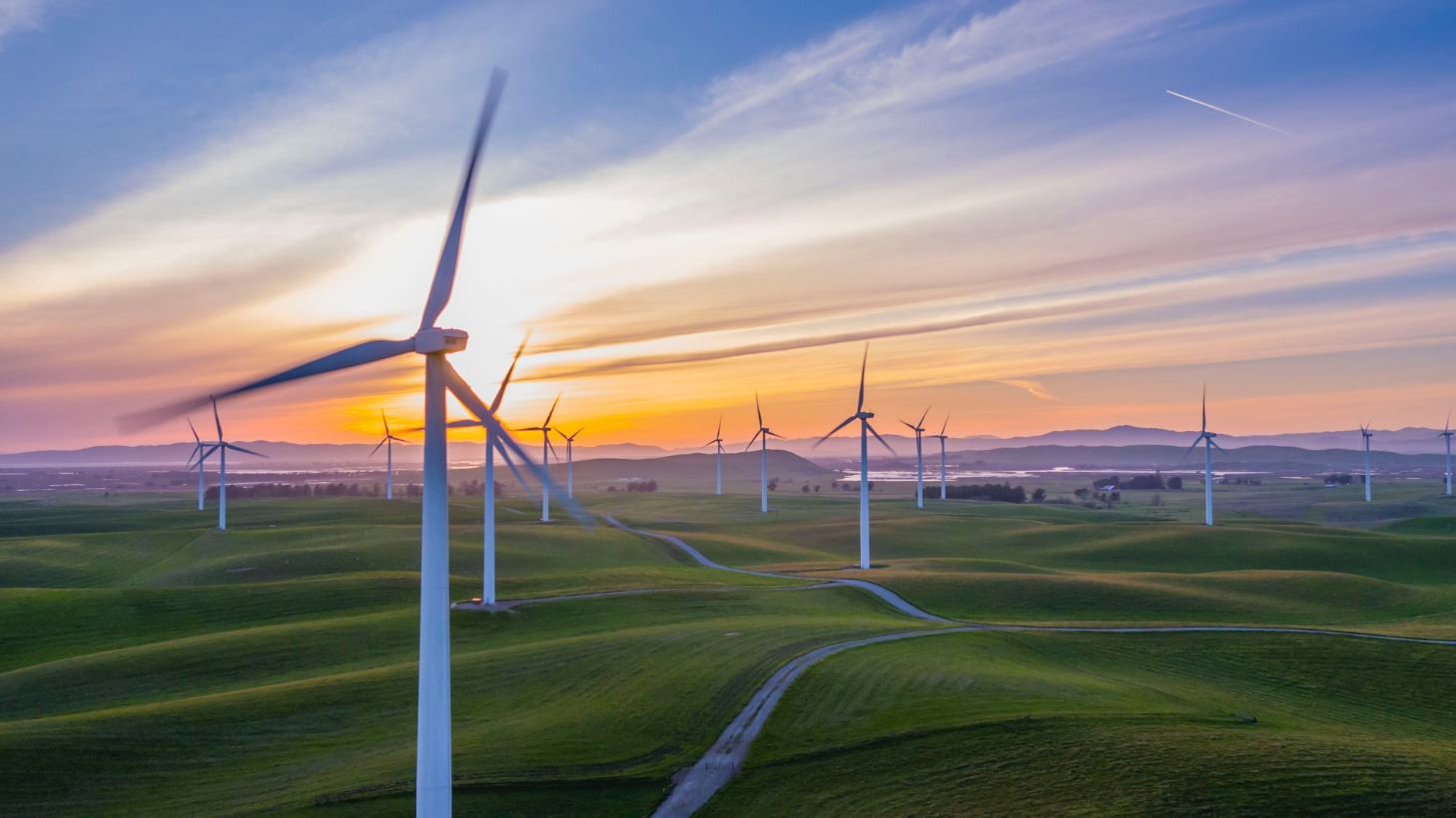 A photo of wind turbines in front of an orange setting sun.