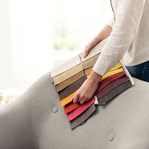 Professional decorator choosing the best upholstery for the armchair by holding fabric samples against it
