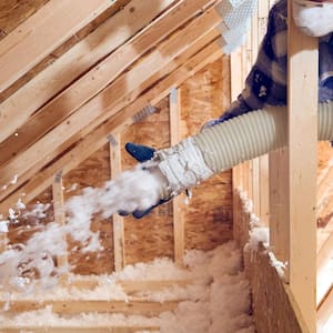 A worker using a blown-in insulation machine to insulate an attic