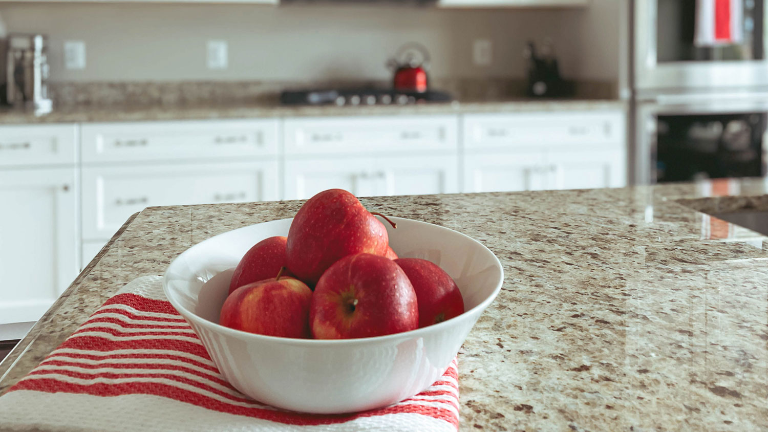 A bowl of apples sits on granite countertops