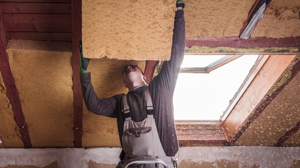 A man installing large blocks of insulation in a ceiling