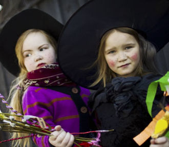 Two children dressed as witches with a bunch of decorated willow twigs in hand.