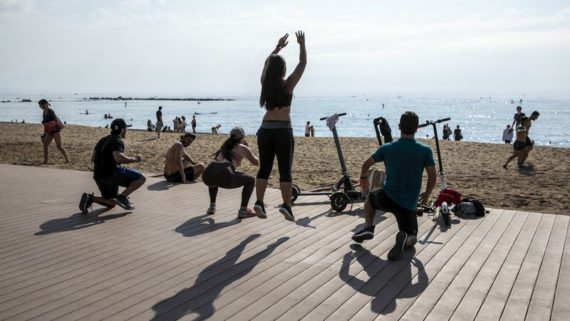 Jovent fent exercici a la platja, amb els patinets elèctrics aparcats. 