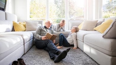 A grandfather sitting on the carpet reading a book to his grandchildren