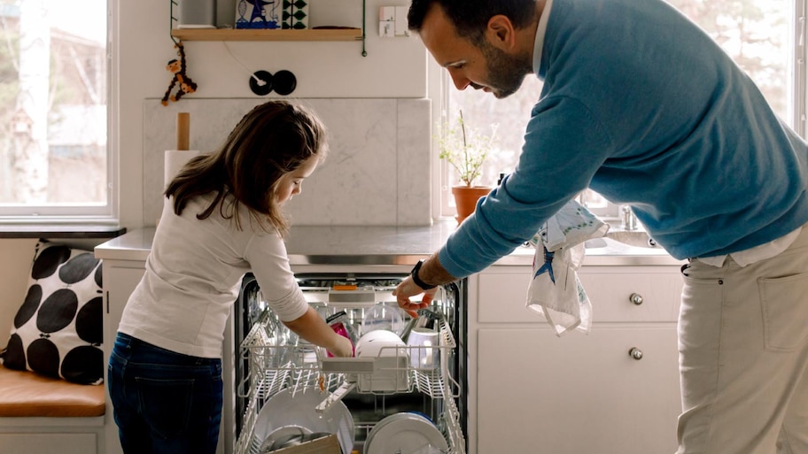 Father and daughter arranging utensils in dishwasher at kitchen