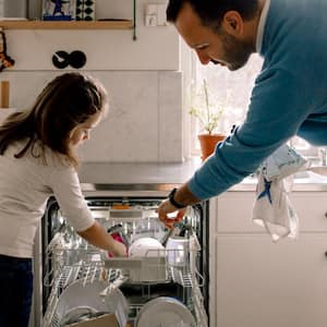 Father and daughter arranging utensils in dishwasher at kitchen