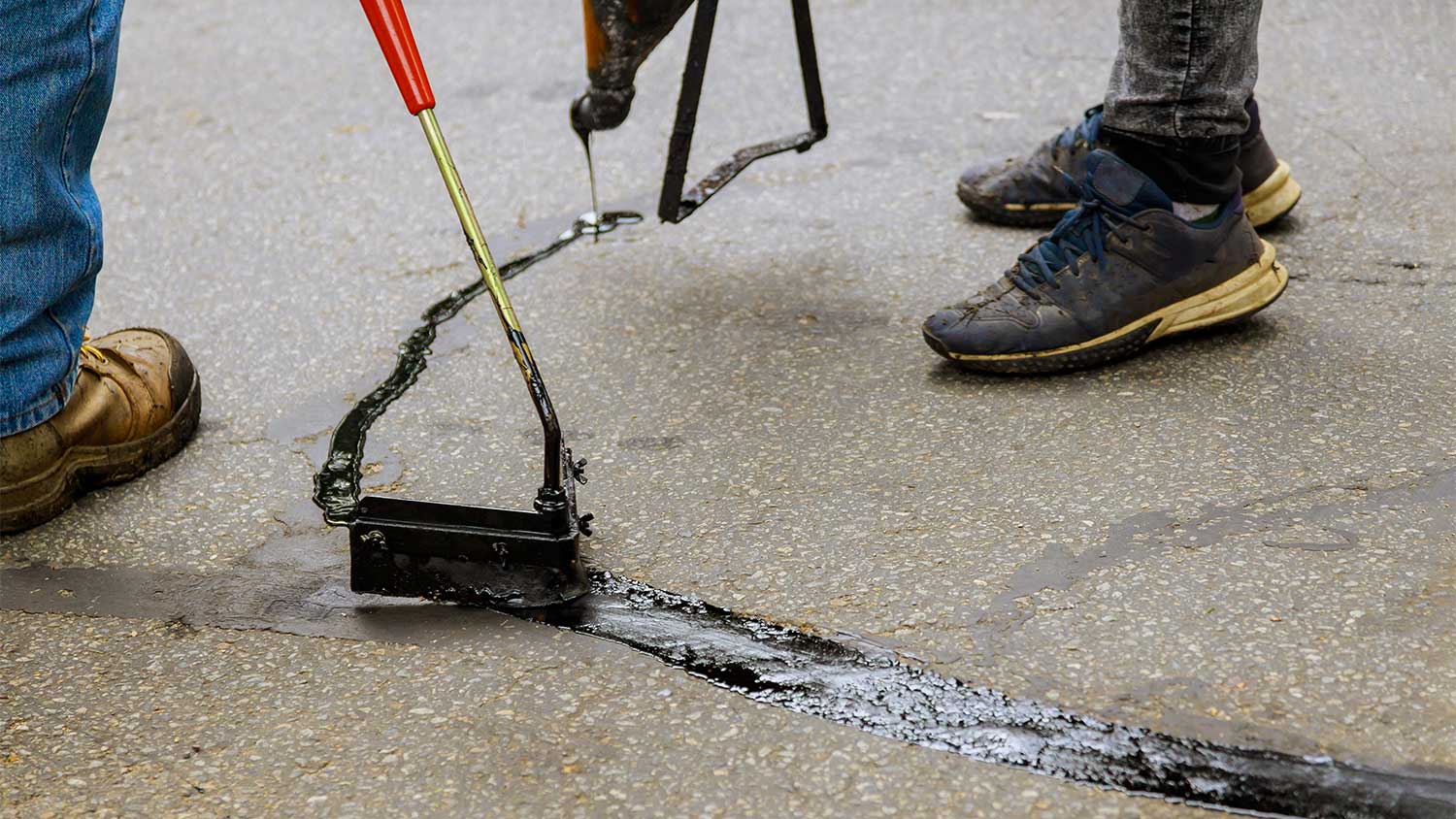 closeup of two workers patching cracks on the driveway