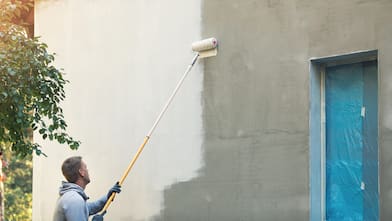 A professional painting a house wall with a roller
