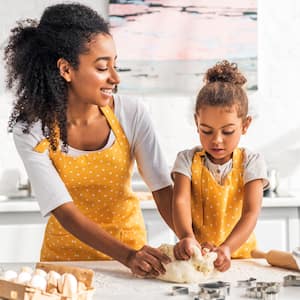 Mom and daughter in yellow polka dot aprons kneading dough on the kitchen counter 