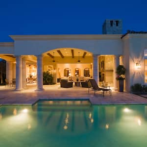 The exterior of a villa with lanterns on the walls and a lit swimming pool