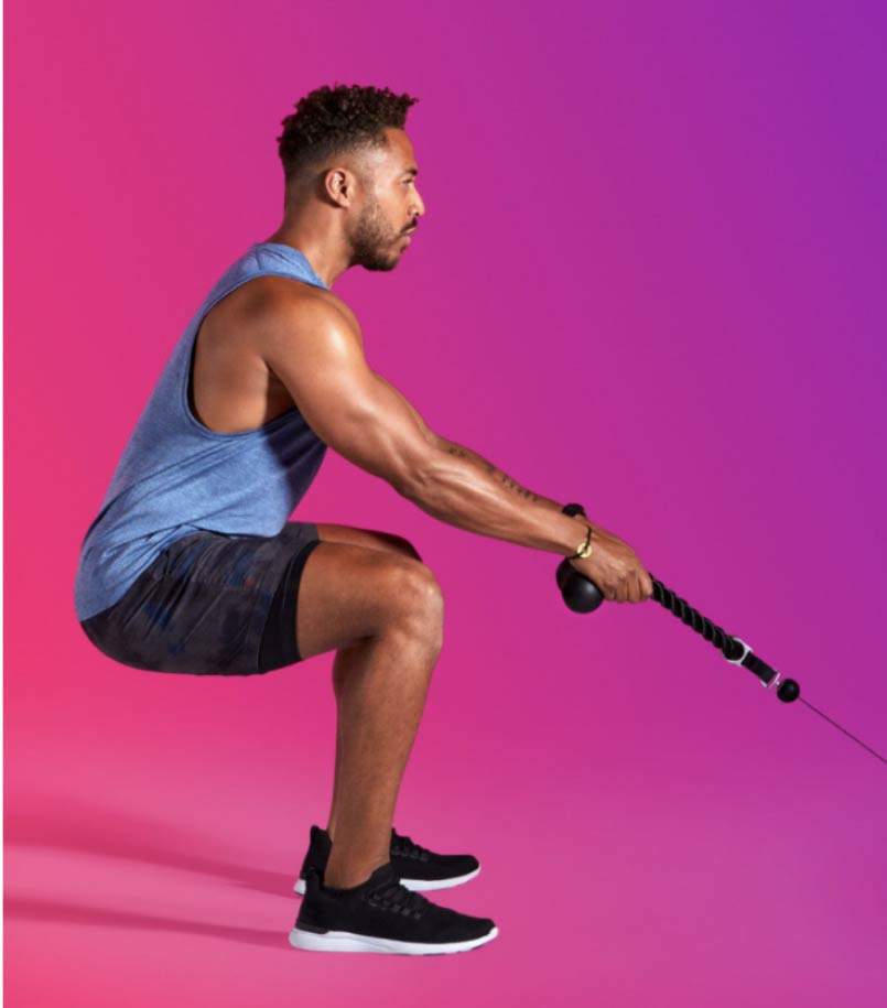 A man in workout clothes performs a squatting workout with a Tonal smart home gym machine on a multi-color backdrop.