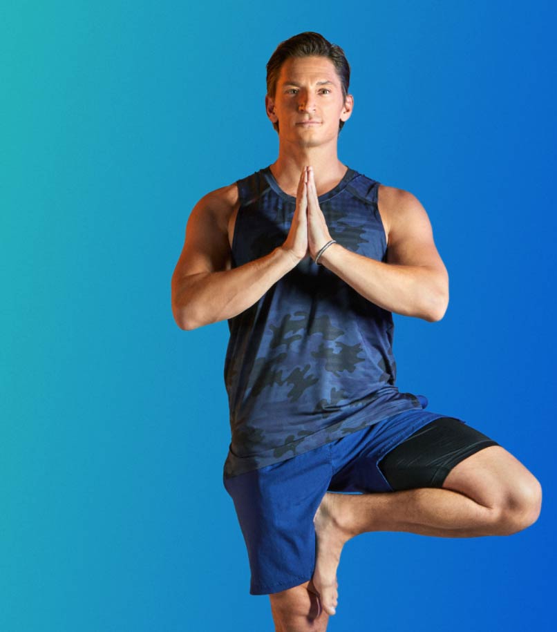 A man in workout clothes performs a yoga pose against a blue backdrop.