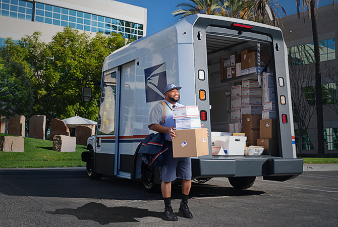 Letter carrier ready to deliver packages unloaded from the back of a USPS Next-Generation Delivery Vehicle.