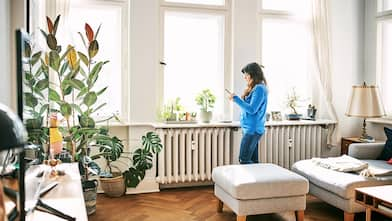 Woman stands by living room radiator looking at phone