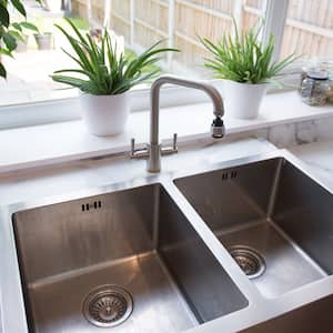 A stainless steel twin sink with marble countertop and view to the backyard