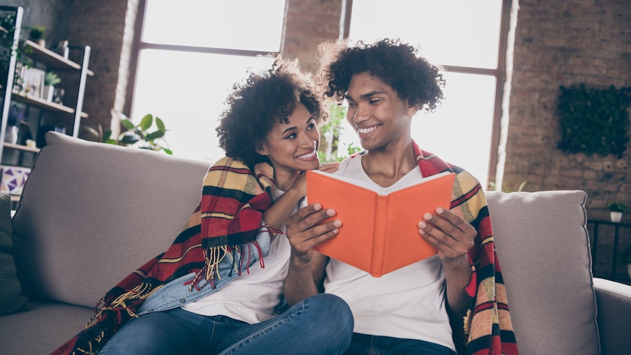 A young couple reading a book covered in a blanket