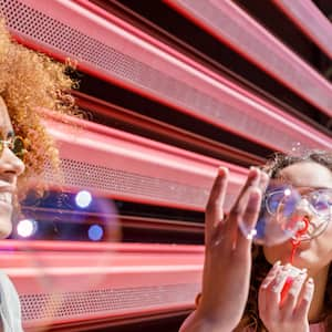 Female friends playing with bubbles in front of a corrugated fence