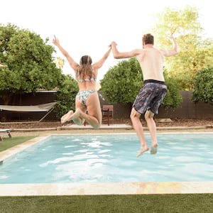A man and woman jumping into a backyard inground pool together
