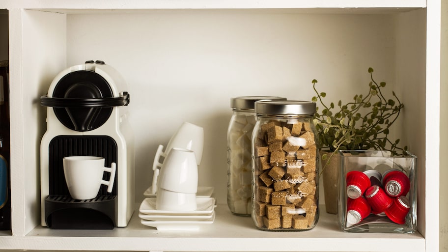 White coffee maker and storage containers on kitchen pantry shelf