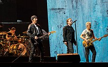 A color photograph of members of the band U2 performing on stage