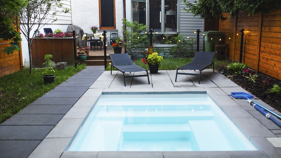 A small backyard with a small, square swimming pool surrounded by concrete tiles