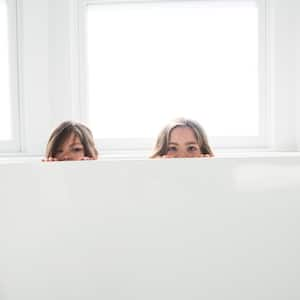 Two sisters peeking over the edge of bathtub