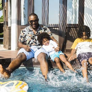 A family sits on the edge of a swimming pool