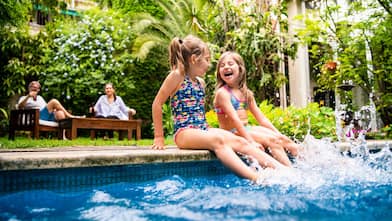 Little girls sitting at poolside splashing water 