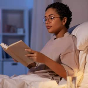 A young woman reading a book in bed at night