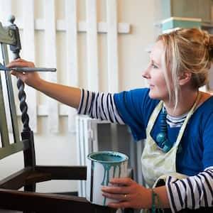 Woman painting wooden vintage chair with a brush