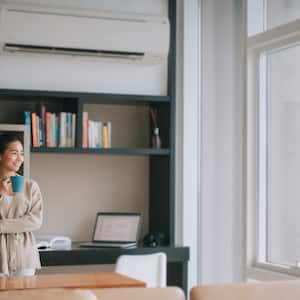 woman with cup of coffee near large windows and underneath air conditioning vent