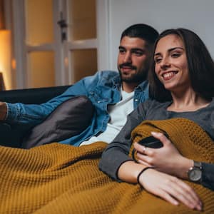 A young couple covered in a blanket watching tv