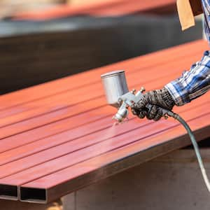 Worker spraying paint to steel pipe