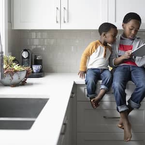 Two kids sit on kitchen counter while looking at ipad