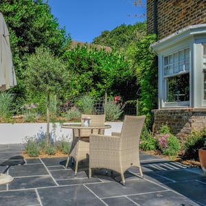 A backyard bluestone patio with an umbrella and wicker patio set