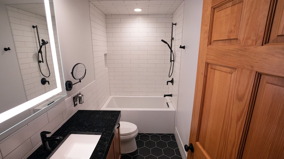 Bathroom with black honeycomb tile floor, black vanity, matte black fixtures, subway tile shower wall, and lighter mirror