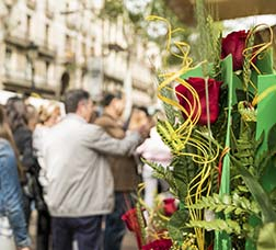 Gent caminant per la Rambla amb una parada de roses en primer terme 