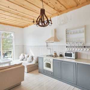 Kitchen with gray cabinets, whitewashed wood walls, 2 iron chandeliers hanging from a wood ceiling, and a nearby dining room 