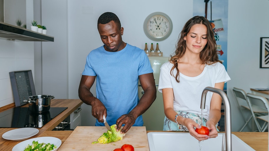Couple rinses vegetables and prepares salad in kitchen