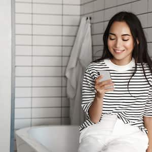 woman sitting on bathtub looking at her phone