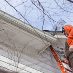 man on ladder removing animal from gutter on roof 