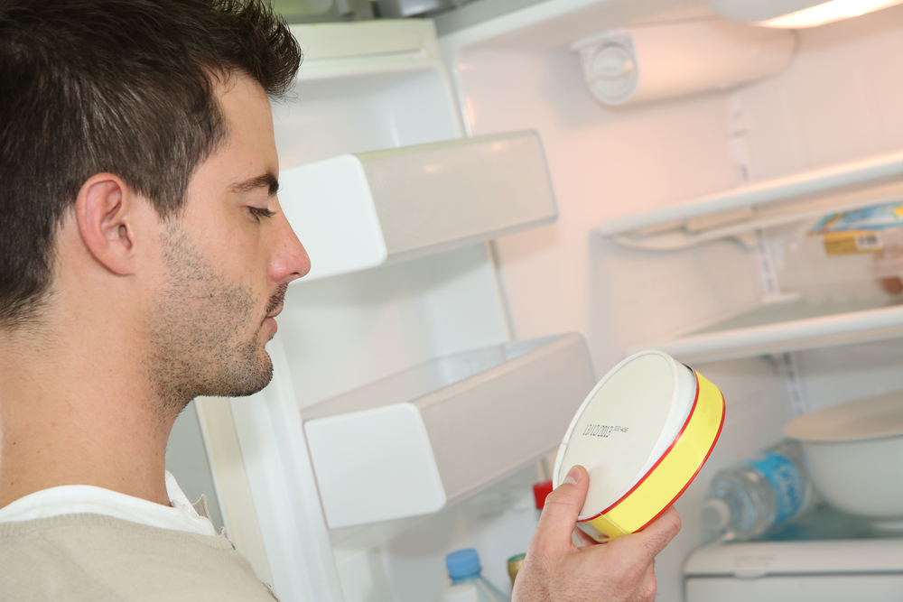 A man looks closely at the expiration date of food in his fridge.