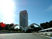 A photo showing the Malaysian Parliament building along with 2 white arches in diagonal position front of the building.