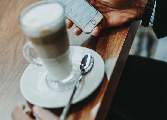 person holding phone and reading his emails with coffee