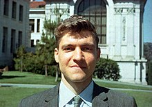 A man in a suit faces the camera while he stands in front of a building.