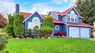 view of bright blue suburban home with green yard and landscaping