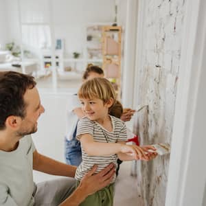 A father, mother, and two small children whitewash a brick wall in their living room