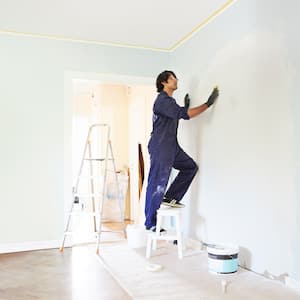 A contractor standing on a ladder while applying plaster on wall