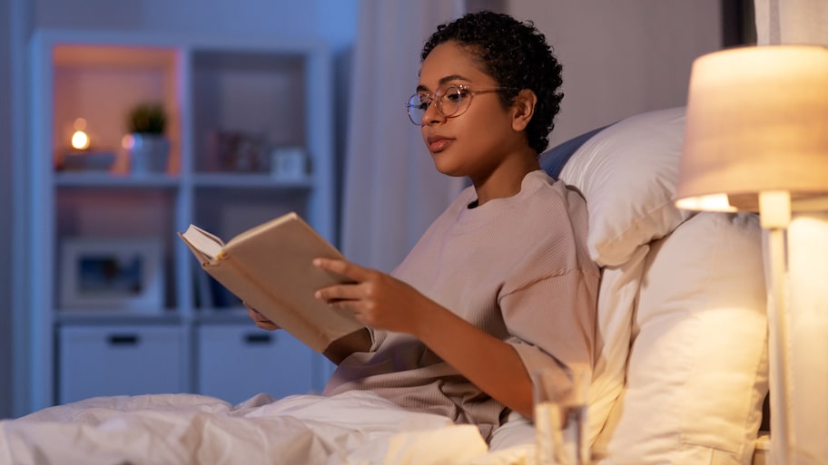 A young woman reading a book in bed at night